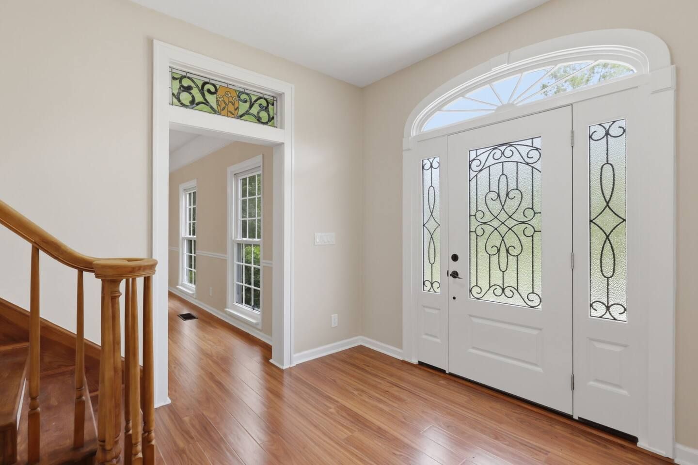 A hallway with wooden flooring, a wooden staircase, and a white door with decorative glass panels.