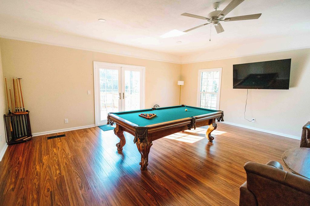 A room with a pool table, ceiling fan, and a television mounted on the wall.