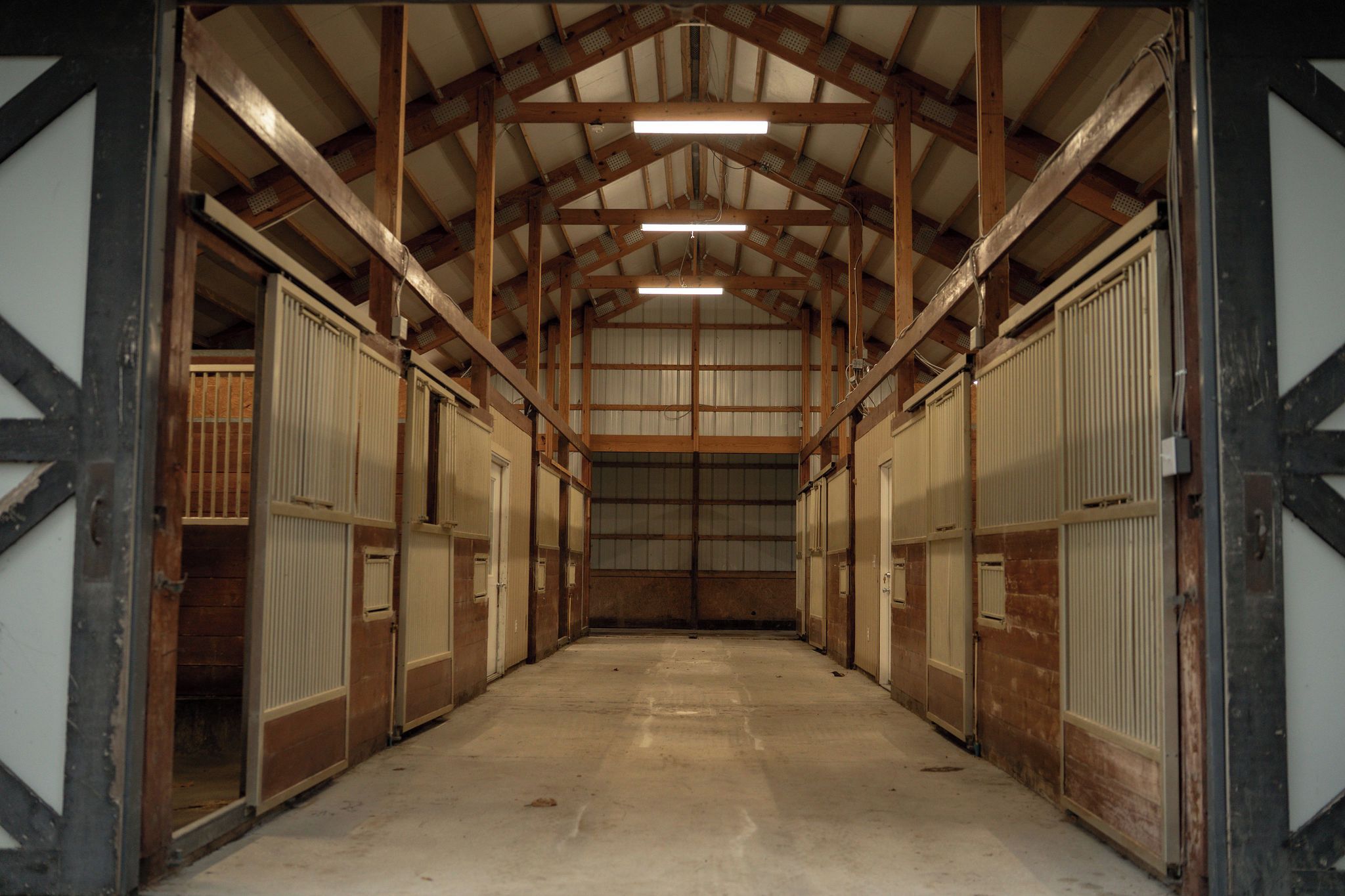 A long, narrow indoor space with a high ceiling and wooden beams, featuring a central walkway and metal doors on both sides.