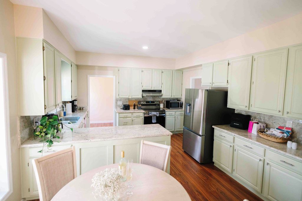 A kitchen with light green cabinets, a marble countertop, and a dining area with a table set for two.