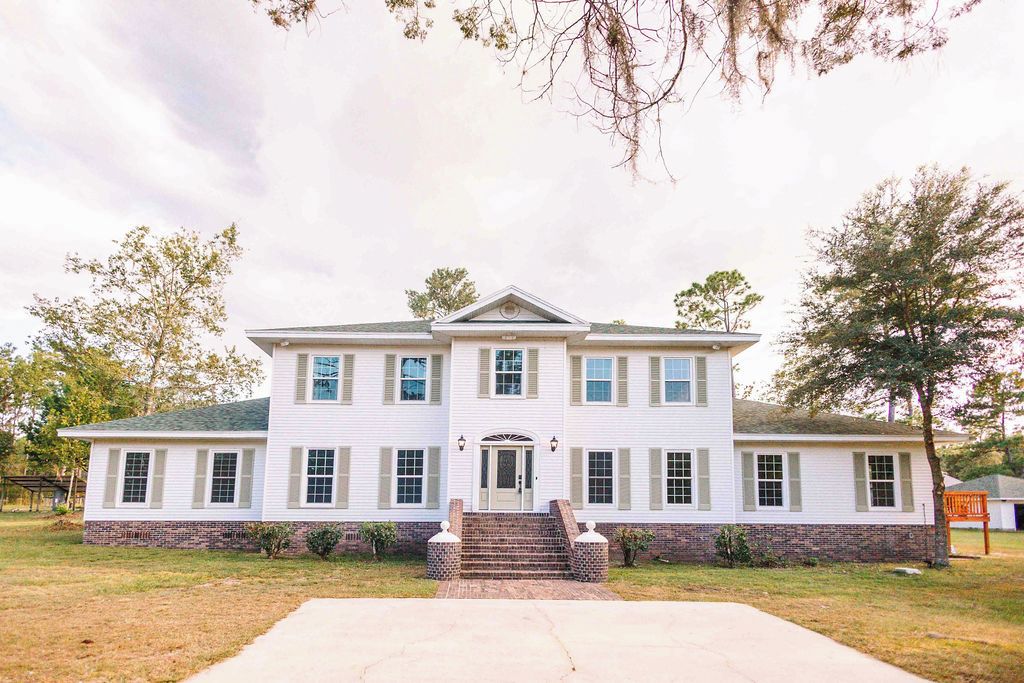 A two-story white building with a symmetrical facade, a central entrance with steps, and a brick foundation.