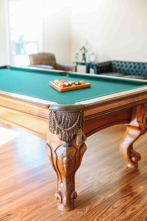 A pool table with a green felt surface, a set of pool balls, and a decorative wooden leg with a tassel.
