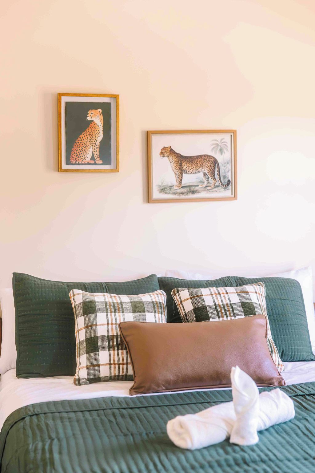 A bedroom with a bed, pillows, and two framed pictures of leopards on the wall.