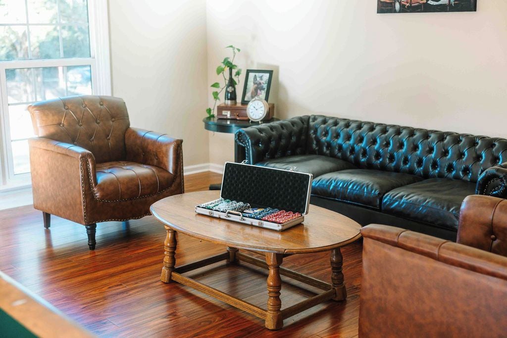 A living room with a brown leather armchair, a black leather sofa, and a wooden coffee table with a laptop.