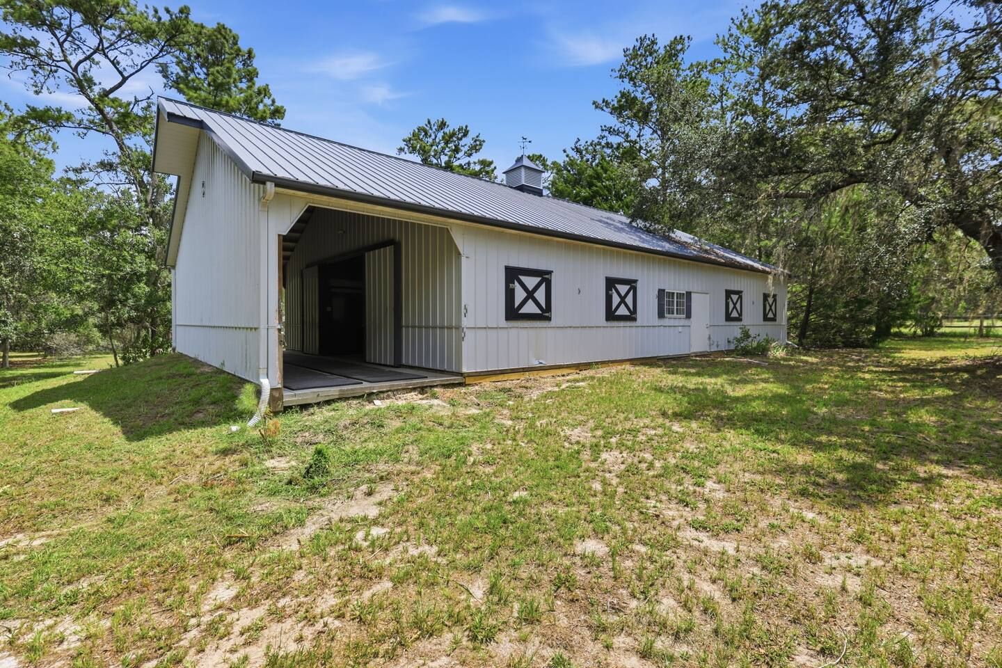 A single-story building with a large open garage door, surrounded by trees and grassy area.