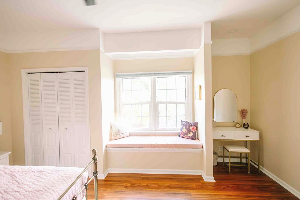 A bedroom with a window seat, a bed, a dresser, and a mirror.