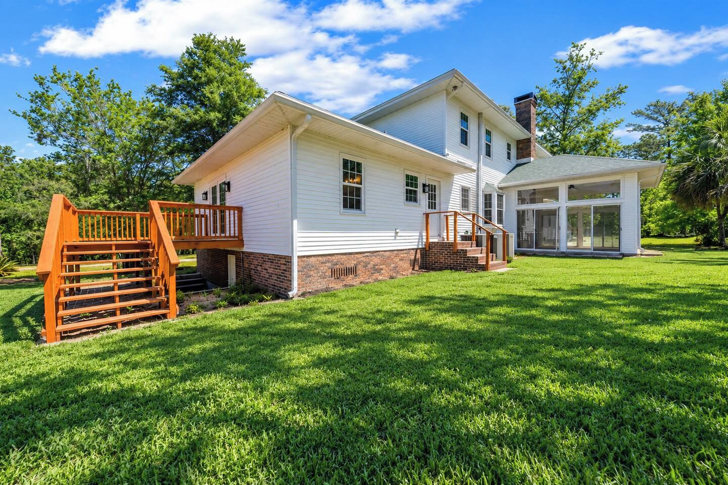Back of the home with deck and a big, open lawn