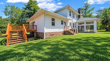 Back of the home with deck and a big, open lawn