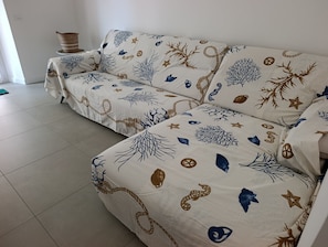 A sofa with a nautical-themed cover, a woven basket on a small table, and a tiled floor. - Apartment 2 minutes from the ocean, public beach, and home amenities (Terracina)