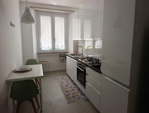 A compact kitchen with a gas stove, a dining table with chairs, and a window with blinds. - Apartment 2 minutes from the ocean, public beach, and home amenities (Terracina)