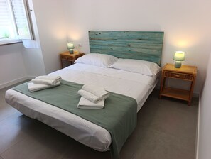 A neatly made bed with white linens and a green throw, two bedside lamps, and a wooden headboard.