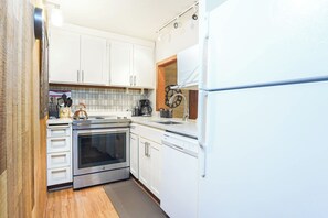 A compact kitchen with white cabinets, a stainless steel oven, a dishwasher, and a coffee maker. - Snowater Forest Nook (Deming)