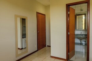 Een gang met twee houten deuren, een spiegel en een badkamer met een wastafel en spiegel.