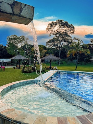 Une piscine agrémentée d’un élément décoratif aquatique, entourée d’une pelouse et d’arbres.