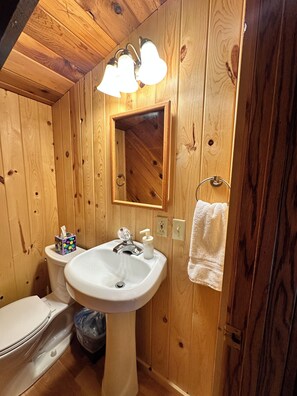 Ein Badezimmer mit Holzwänden, einem weißen Waschbecken, einem Spiegel und einem Handtuchhalter.