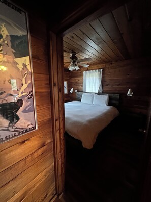 Ein Schlafzimmer einer Holzhütte mit einem Bett, einem Deckenventilator und einem Poster an der Wand.