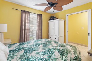 A bedroom with a bed, a ceiling fan, a window with curtains, a white wardrobe, and a door. - Summer Breeze 103 (Miramar Beach)