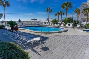 A pool area with lounge chairs and a table, surrounded by a wooden deck and palm trees. - Summer Breeze 103 (Miramar Beach)