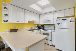 A kitchen with white cabinets, a microwave, a stove, and a refrigerator. - Summer Breeze 103 (Miramar Beach)
