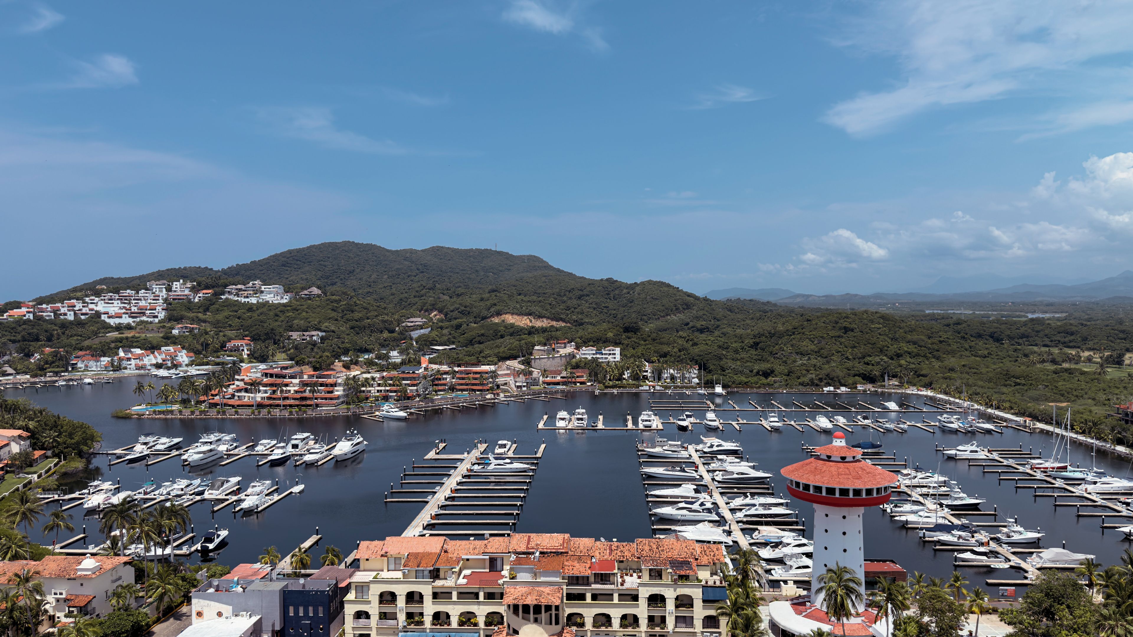 A marina with numerous boats docked, surrounded by residential buildings and a hill in the background.