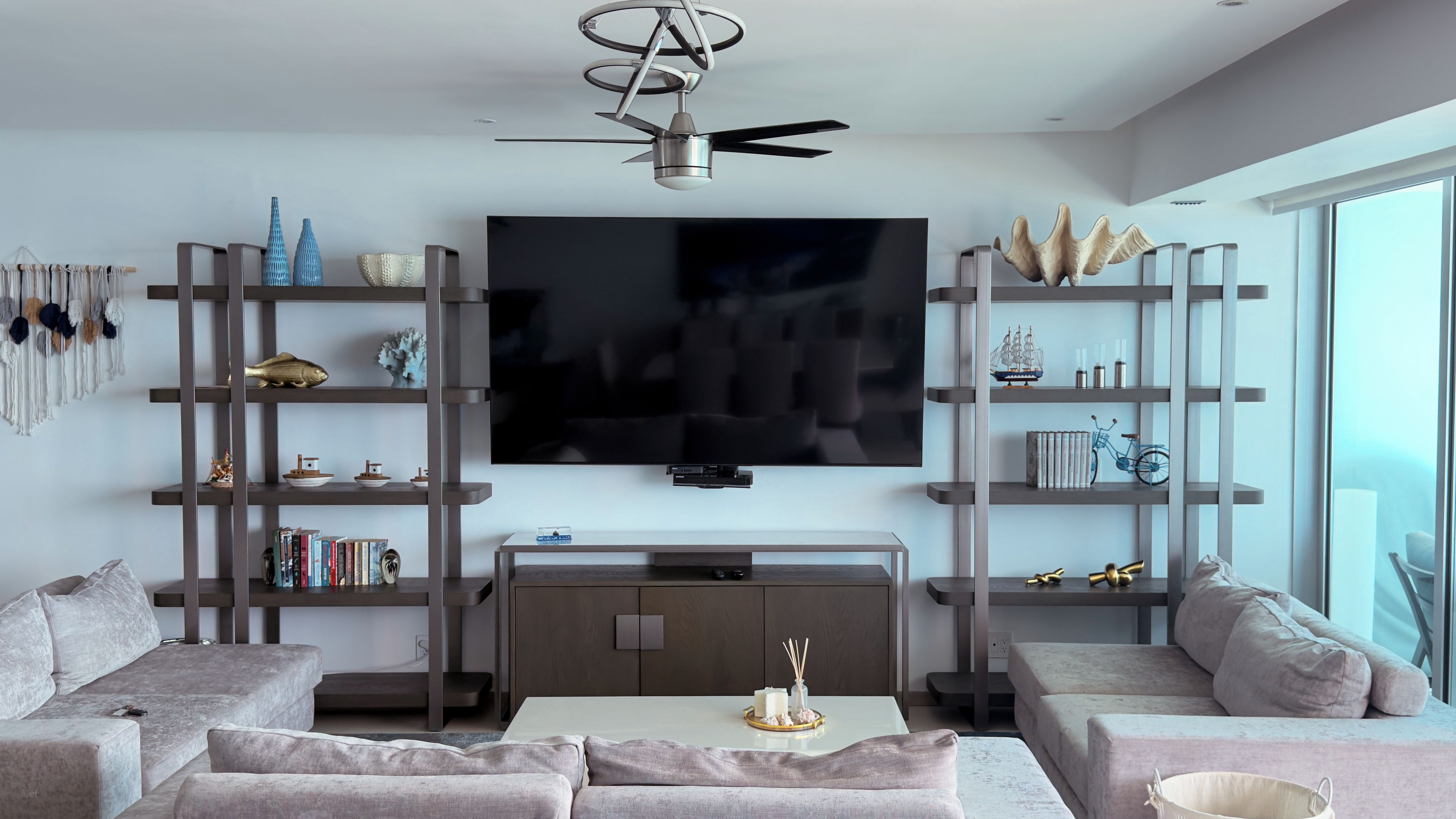 A modern living room with a flat-screen TV, sofas, a coffee table, and decorative items on shelves.