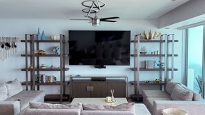 Una sala de estar moderna con televisor de pantalla plana, sofás, una mesa de centro y objetos decorativos en estanterías.