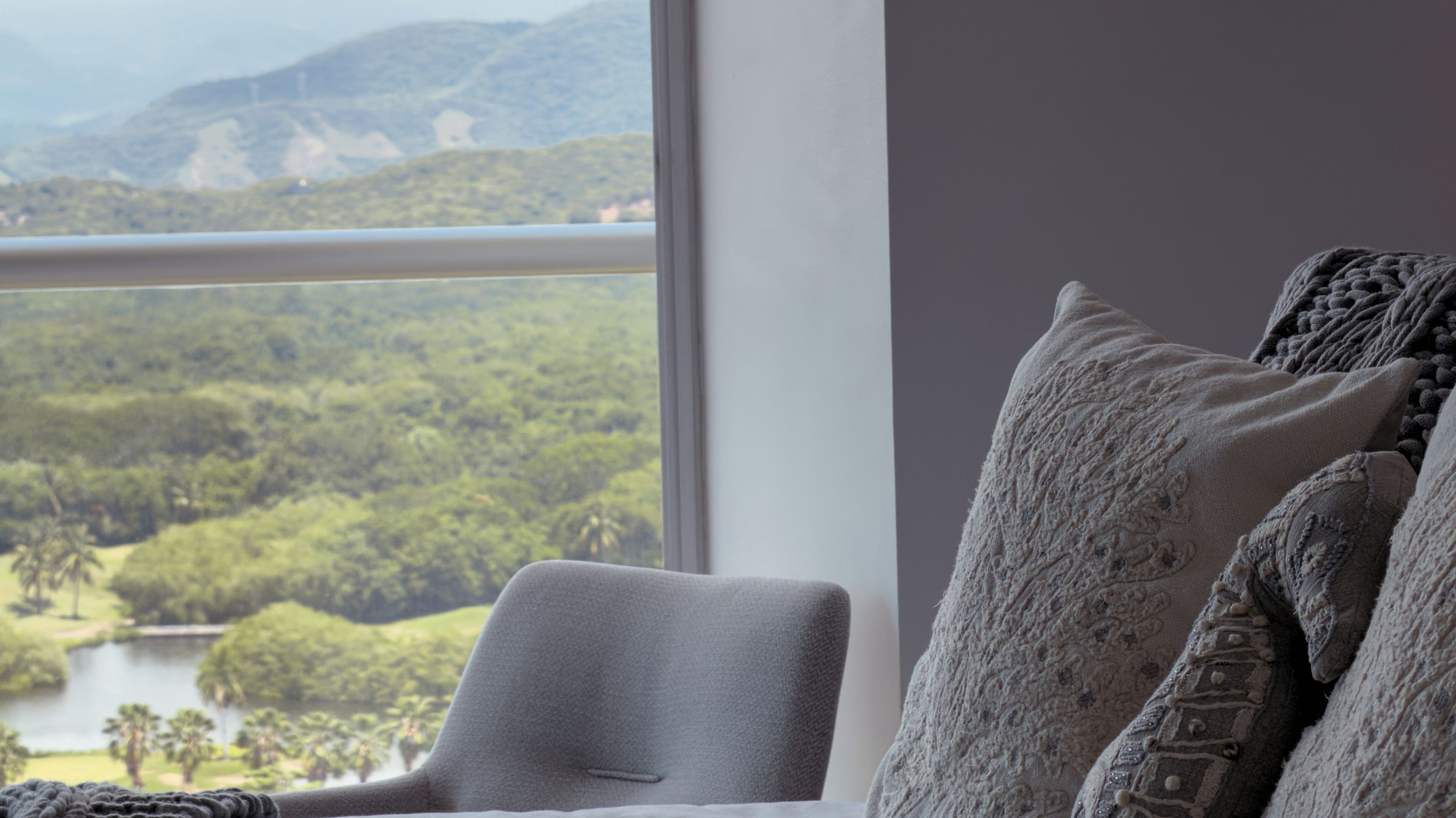 A room with a view of a lake and hills, a window, and a chair with a cushion.