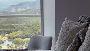 Habitación con vistas a un lago y colinas, una ventana y un sillón con cojín.