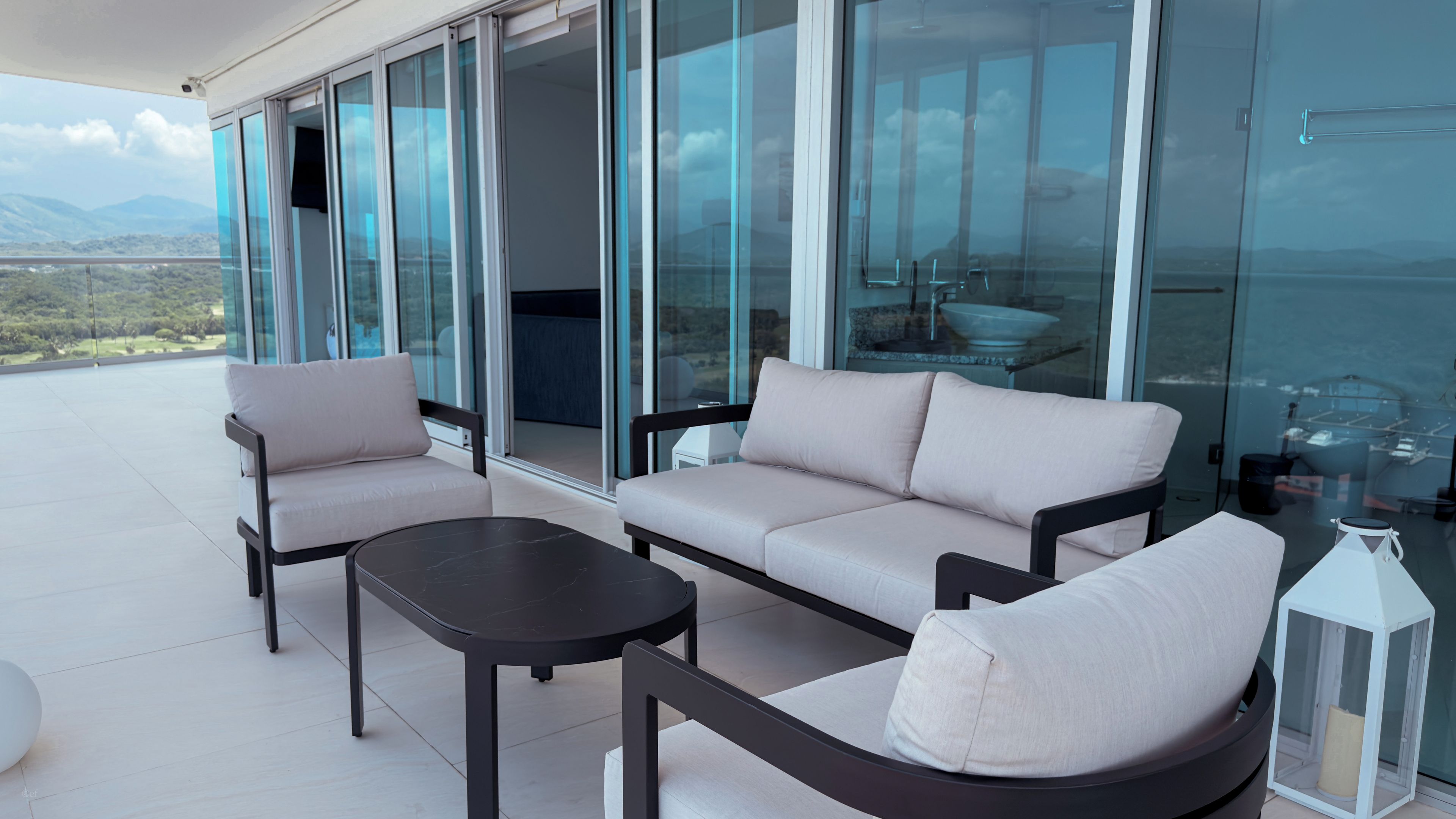 Un espace extérieur moderne aménagé avec un canapé et des fauteuils, une petite table et une lanterne.