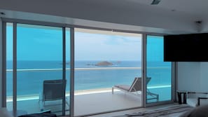 A modern hotel room with a large sliding glass door leading to a balcony with a view of the sea and a small island.