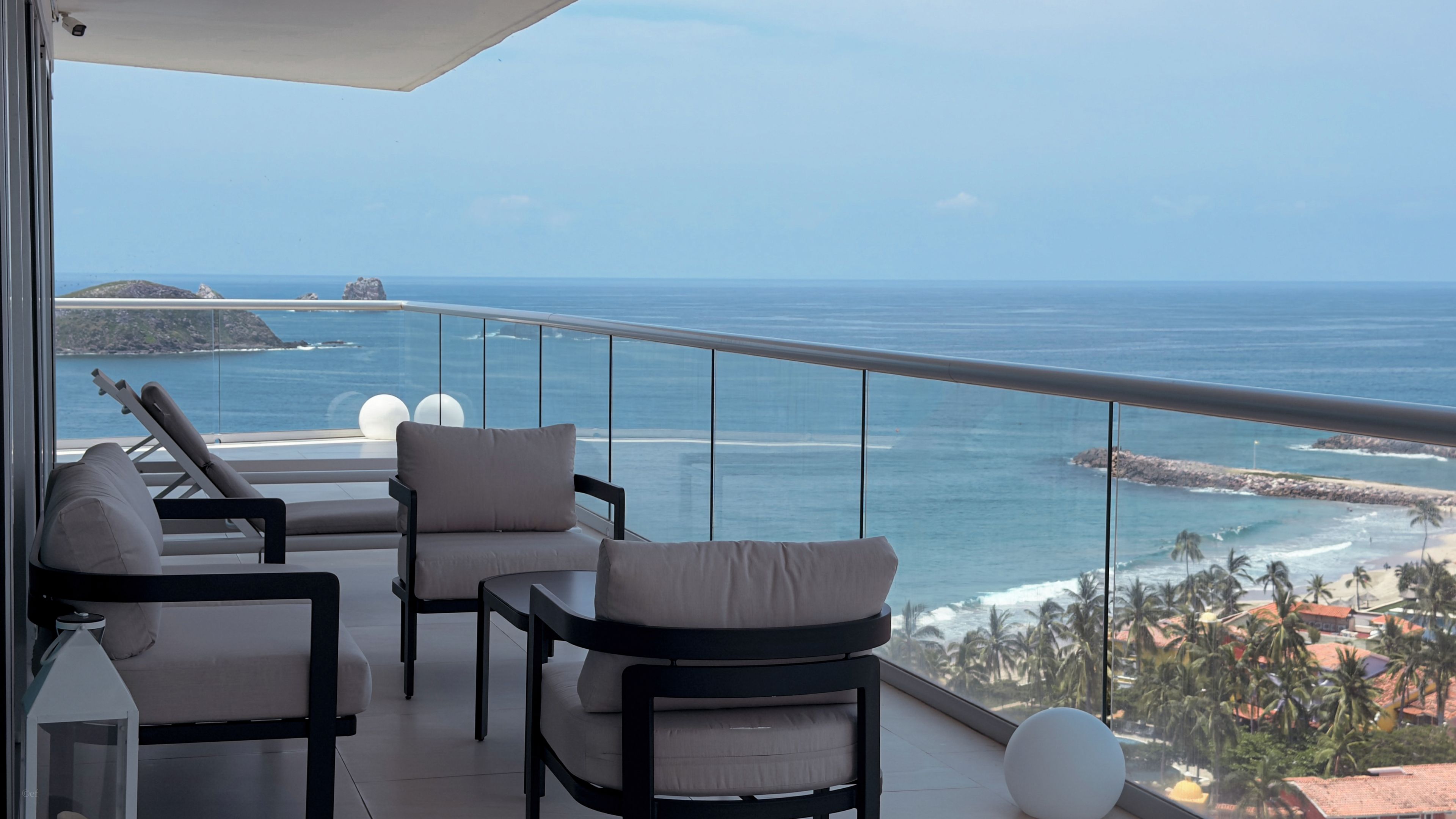 Un balcón con vista al océano, que cuenta con una zona de estar con sillas y una mesa.