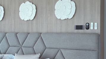 Une chambre à coucher moderne avec une tête de lit capitonnée, une table de chevet en bois dotée de tiroirs, une petite table d’appoint et un ventilateur de plafond.