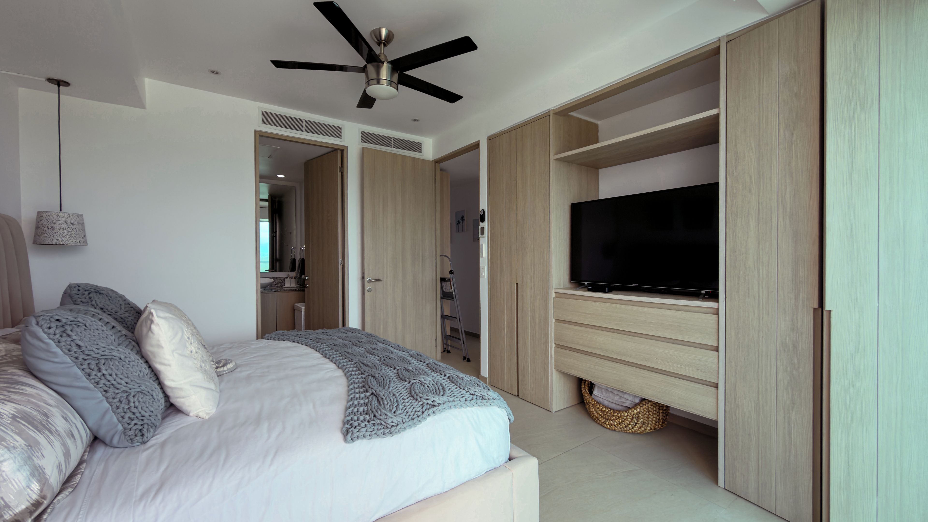 A bedroom with a bed, a ceiling fan, a TV, and built-in wardrobes.