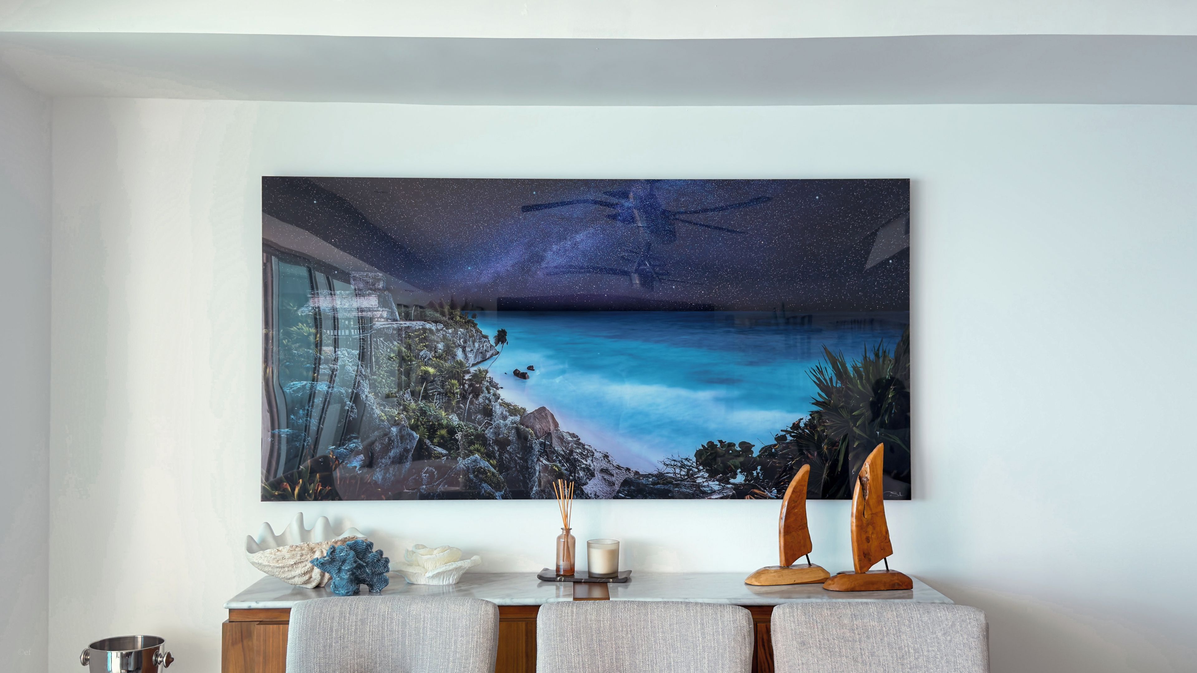 A room with a large painting of a night sky and a beach scene. There is a wooden cabinet with decorative items on it.