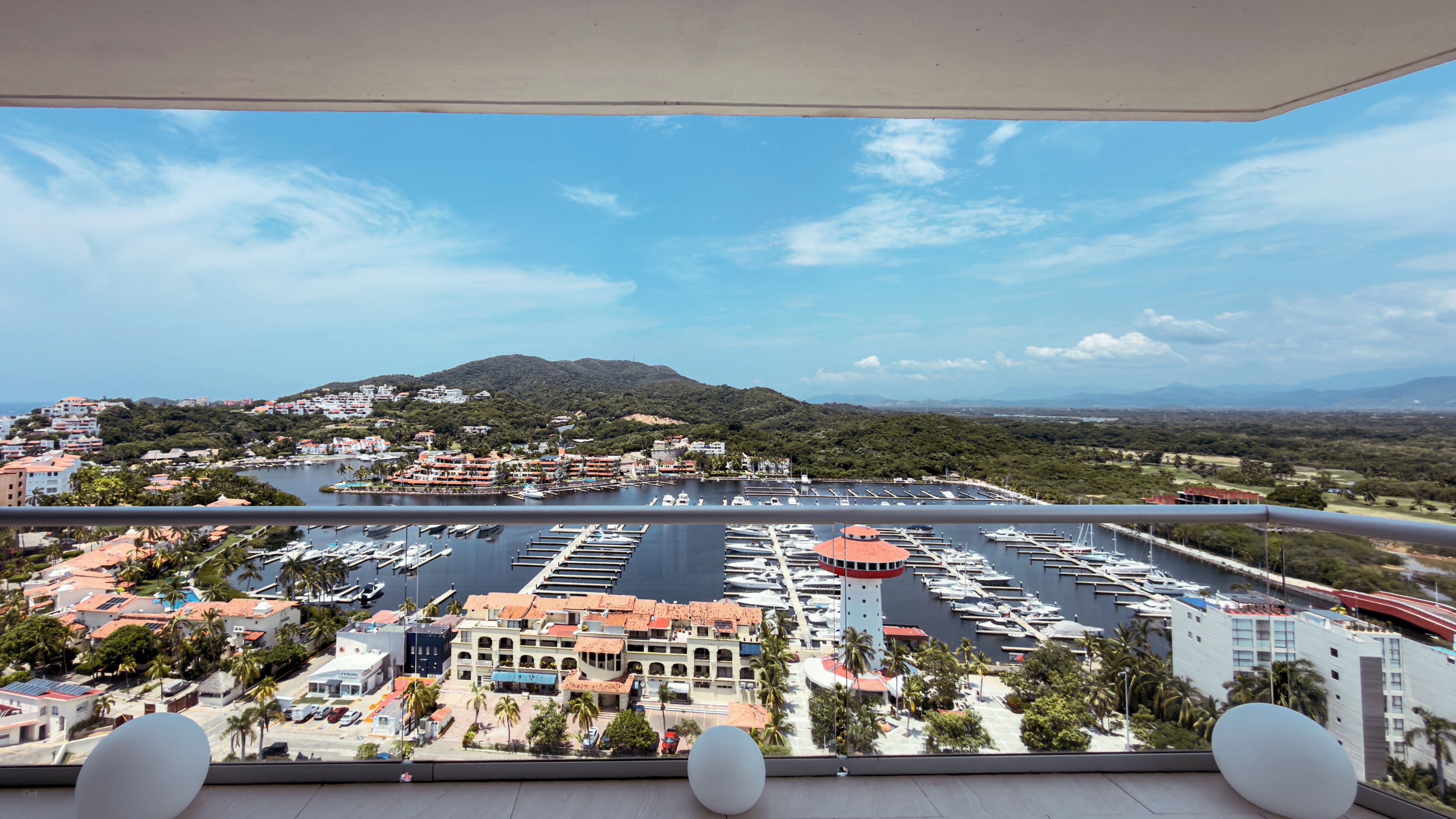 Un balcon avec vue sur un port de plaisance, des bâtiments et une montagne.