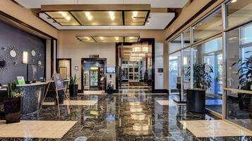 A hotel lobby with a marble floor, reception desk, and a glass door leading to the entrance.