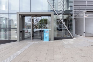 A modern building entrance with a glass door, a blue sign, and a metal staircase. - Vergueiro by Bhomy (São Paulo)