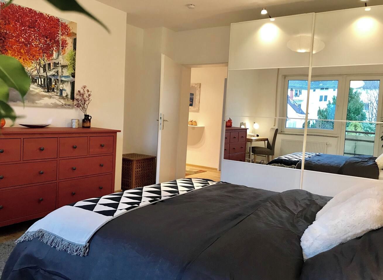 A bedroom with a bed, a dresser, a mirror, and a painting on the wall.
