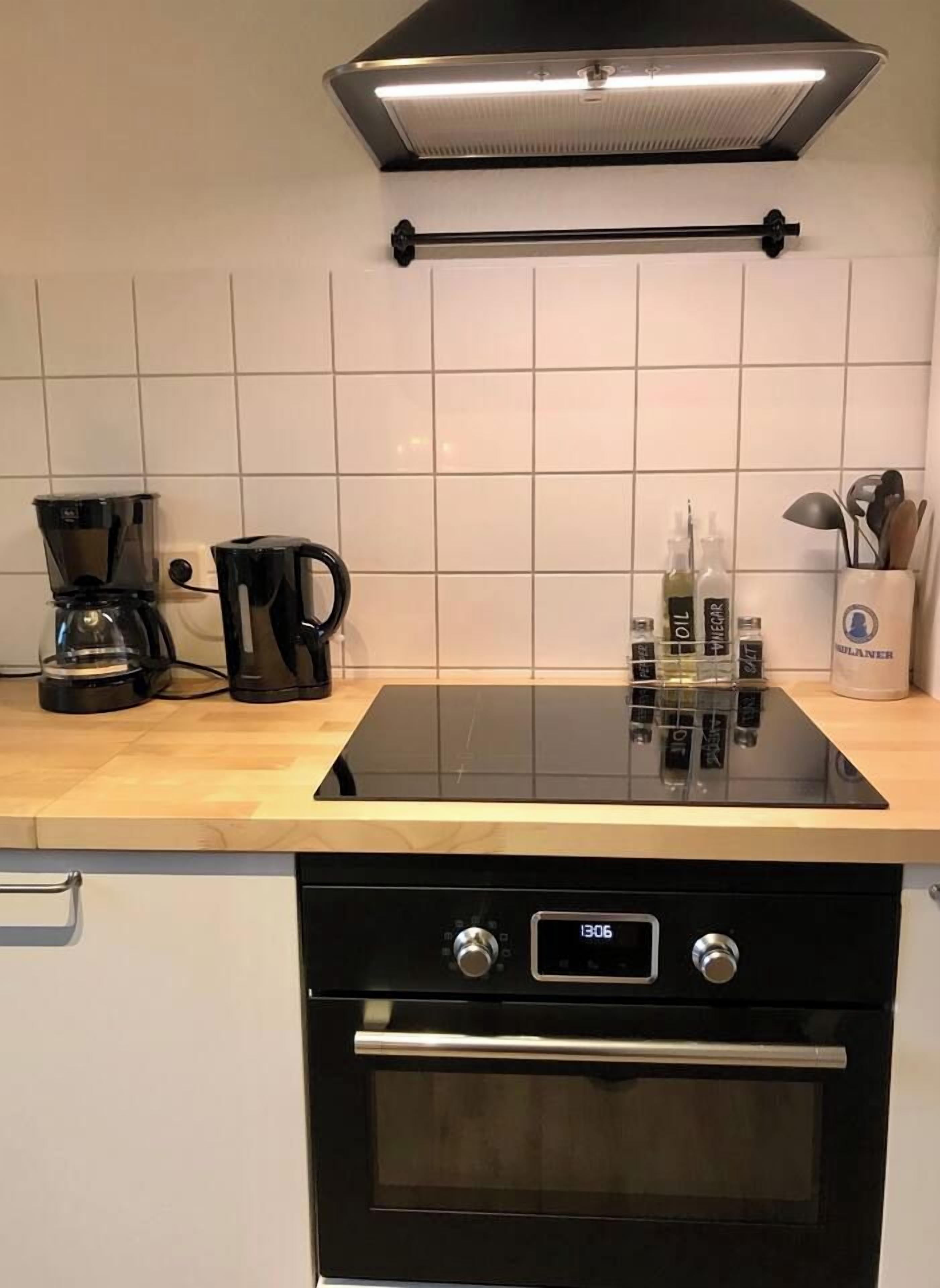 Eine Küche mit einer schwarzen Induktionskochplatte, einer Kaffeemaschine und einer Dunstabzugshaube über der Kochplatte.