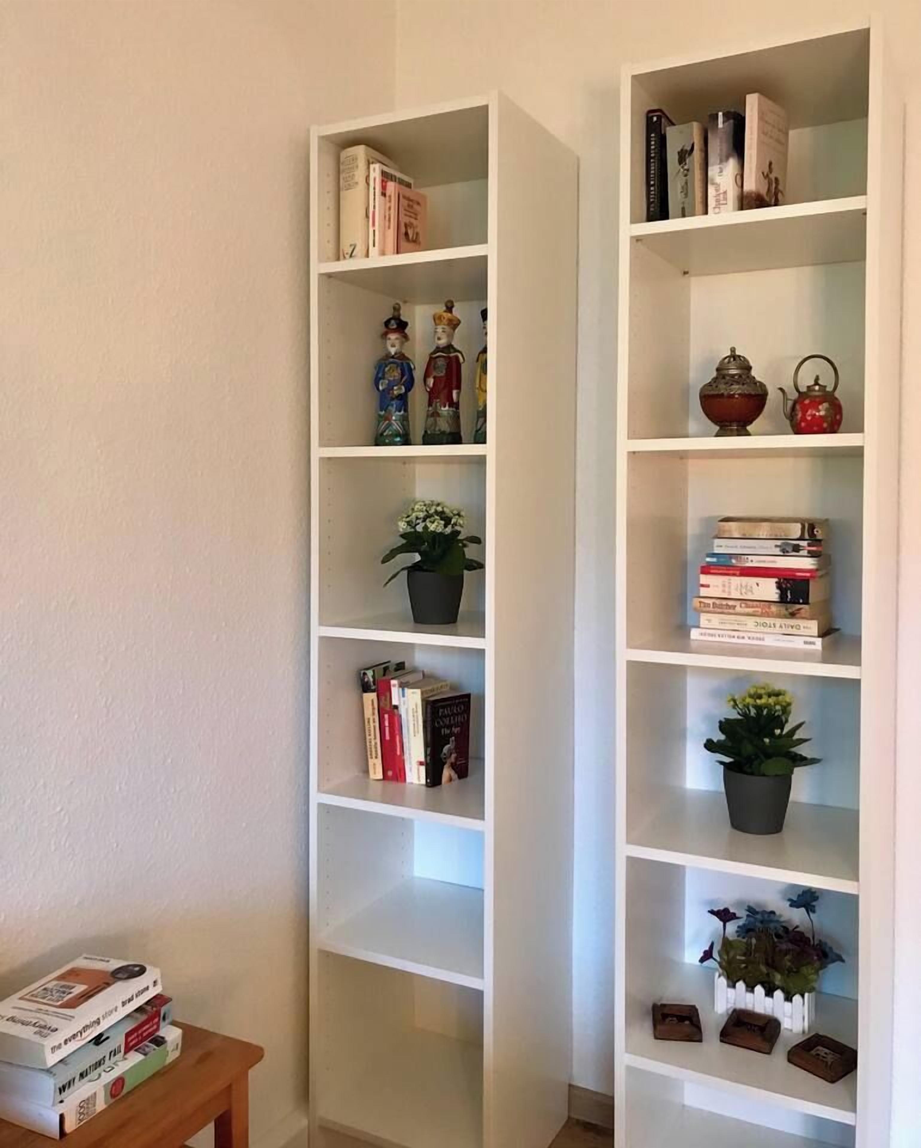 Ein Zimmer mit zwei weißen Bücherregalen, eines mit Figuren, das andere mit Büchern und einer roten Teekanne.