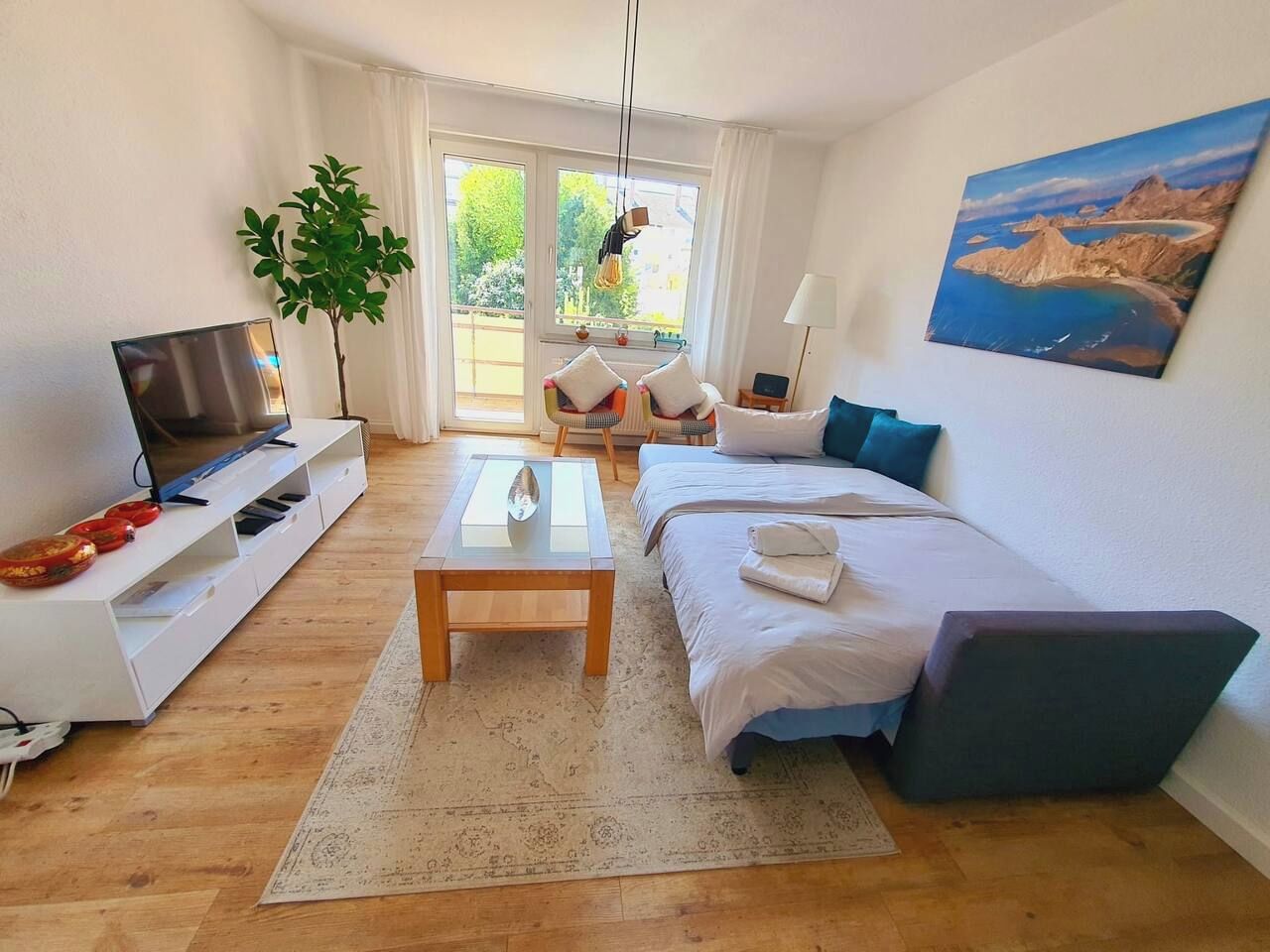 Ein modernes Wohnzimmer mit einer Couch, einem Couchtisch, einem Fernseher und einem großen Fenster mit Blick auf Grünflächen.