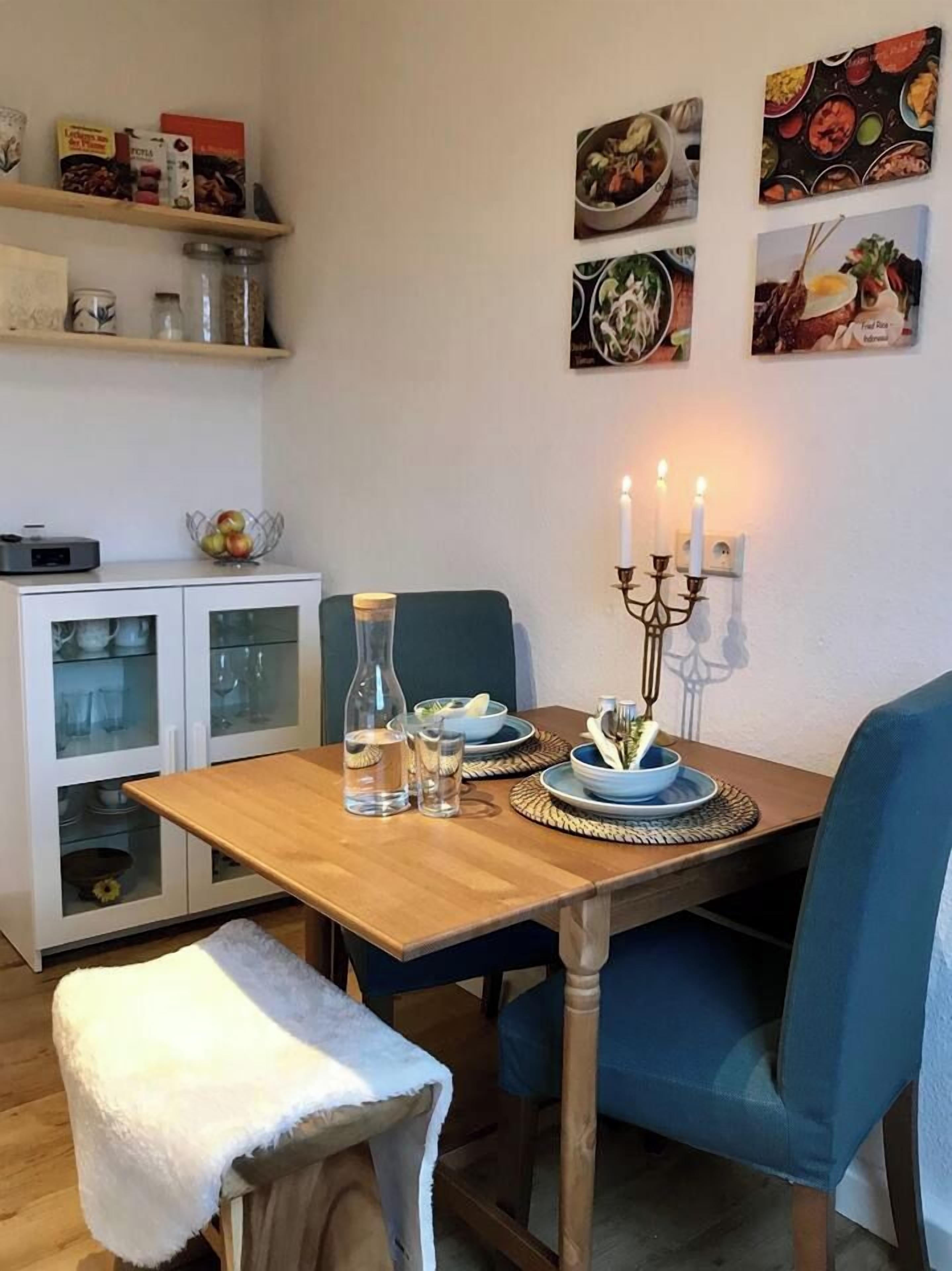 Ein Essbereich mit Holztisch, blauen Stühlen, einem Kerzenhalter und einem Schrank mit Glastüren.