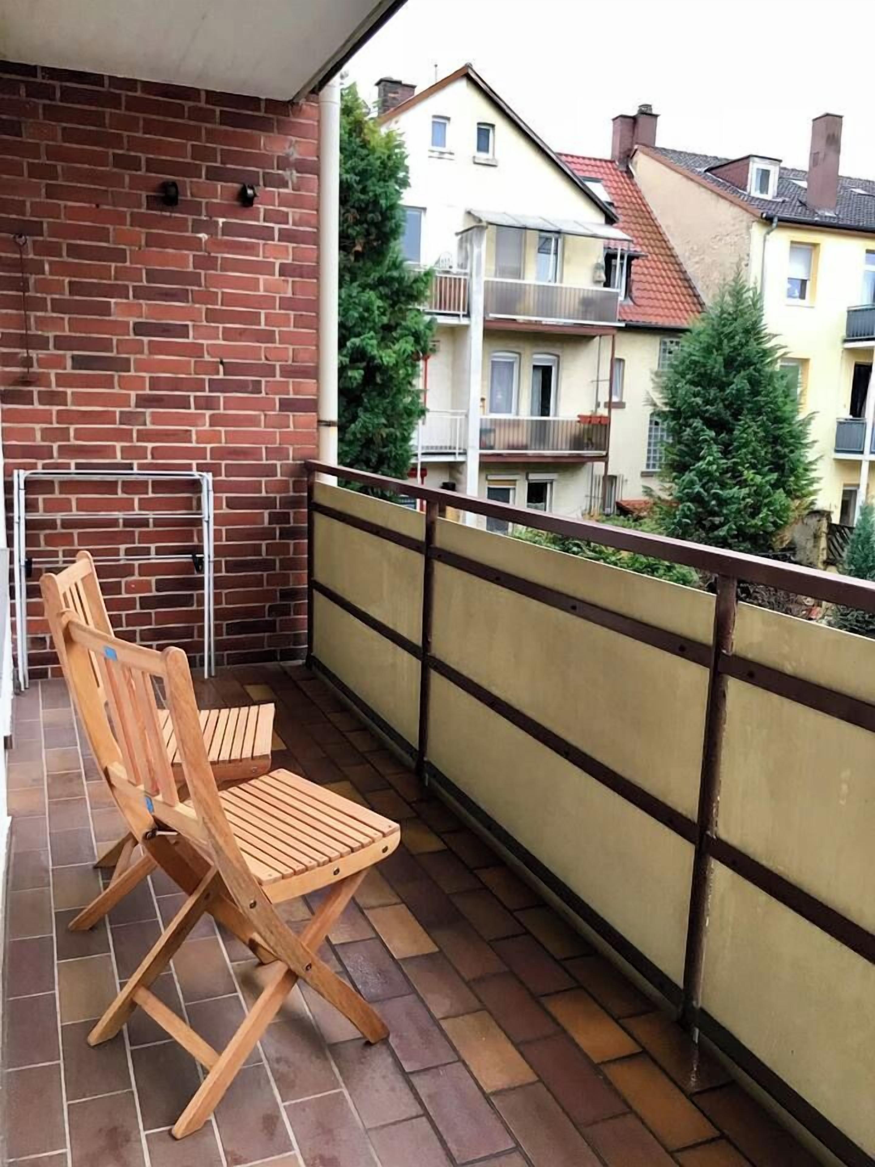 Ein Balkon mit Backsteinmauer, einem Holzstuhl und einem Metallgeländer.