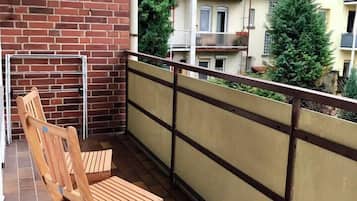 Ein Balkon mit Backsteinmauer, einem Holzstuhl und einem Metallgeländer.