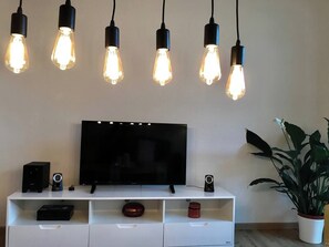 Televisor de pantalla plana sobre un moble blanc amb un altaveu, un objecte decoratiu i una planta en test.