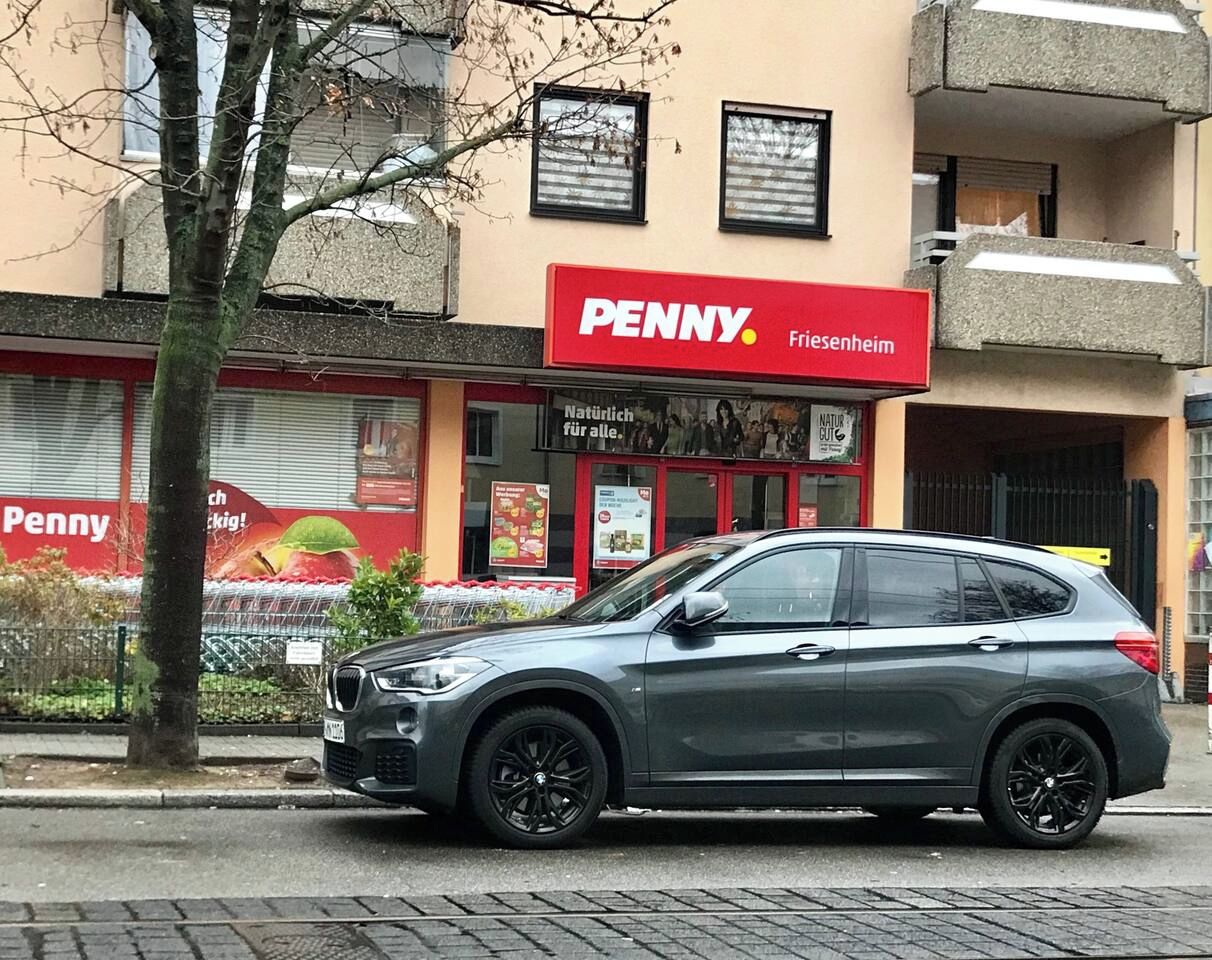 Ein graues Auto vor einem Penny-Markt mit einem roten Schild.