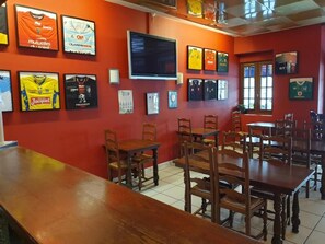 A restaurant with red walls, multiple framed jerseys, a TV, and wooden tables and chairs.