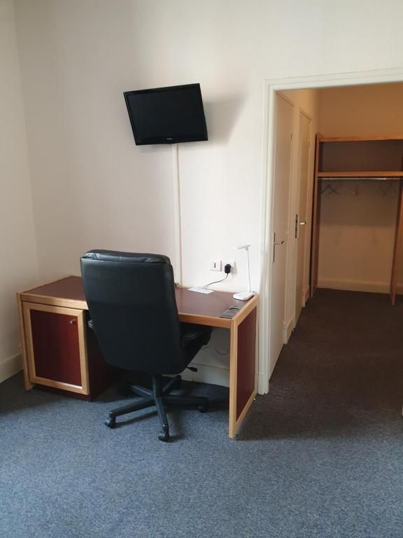 Une chambre équipée d’un bureau, d’une chaise, d’un téléviseur à écran plat fixé au mur et d’une armoire.