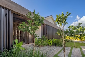 A modern building with a sloped roof, vertical wooden panels, and a well-maintained garden with various plants and a paved walkway. - Villa Flamboyan- Wonderful house in enchanting Casa de Campo (Casa de Campo)