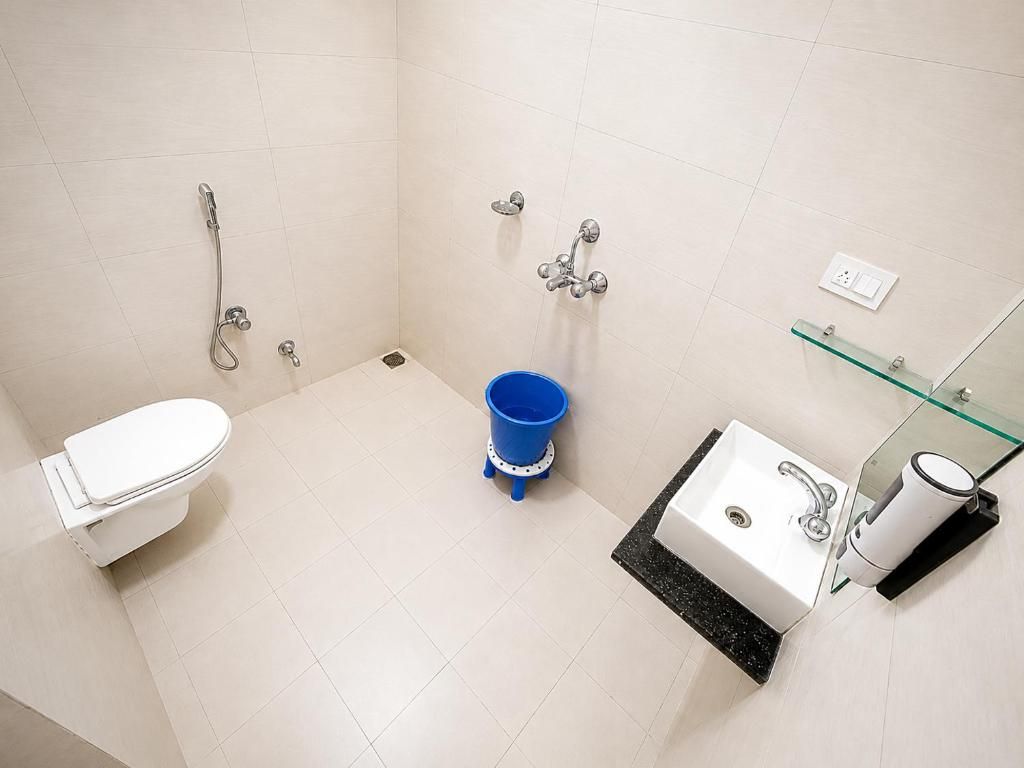 Un baño con inodoro, lavamanos, cabina de ducha de vidrio y un cubo azul.